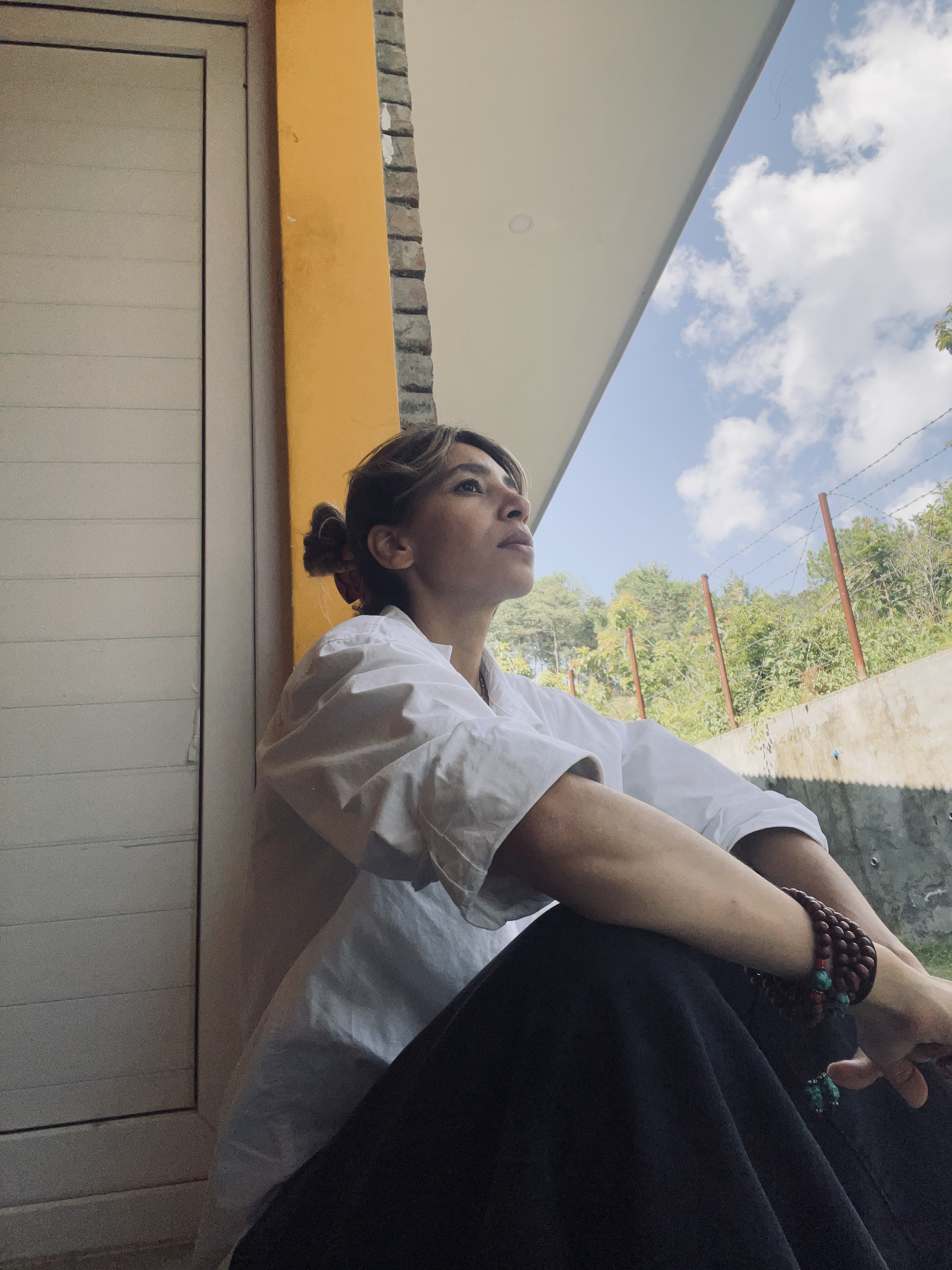 Dr Shima Beigi at the monastery, sitting against a yellow wall in reflection
